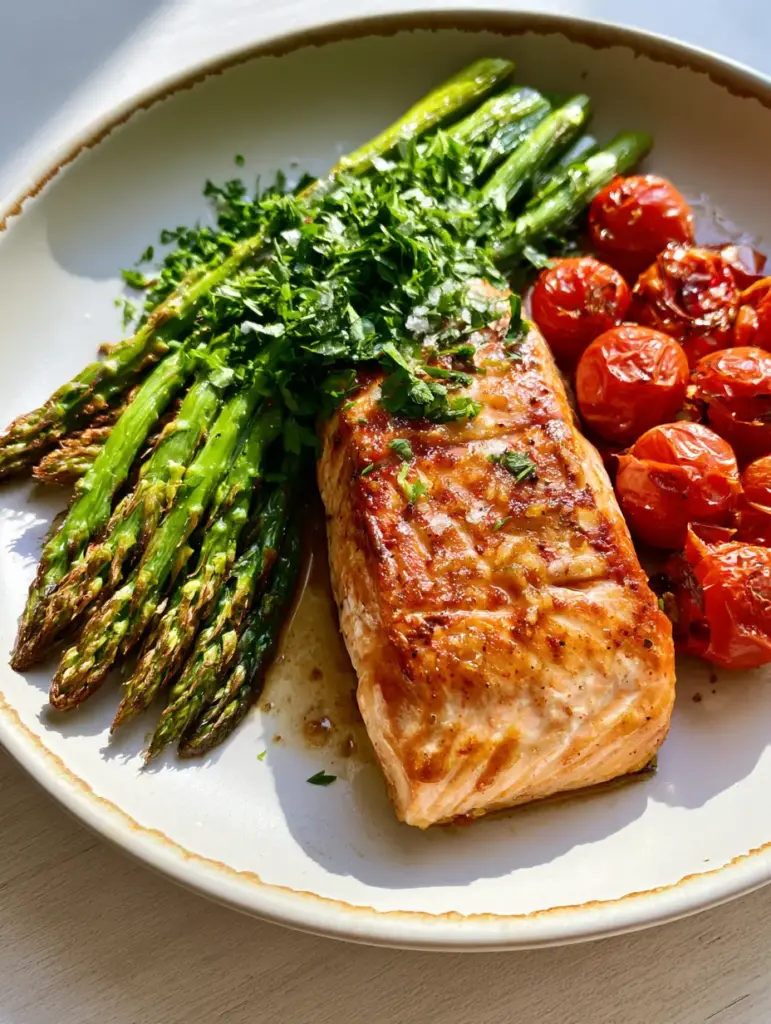 Roasted blistered cherry tomatoes and charred asparagus spears on a matte white plate, a staple side for high protein clean eating meals.